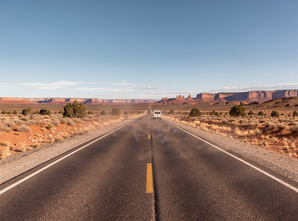 An empty two-lane highway running toward distant red mesas in southern Utah