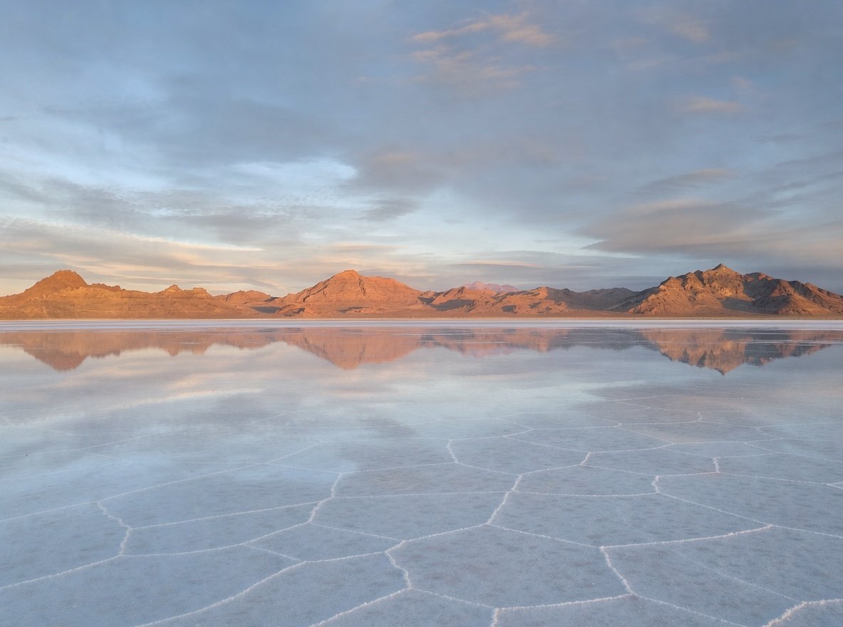 A vast flat expanse of white salt with shallow water reflecting a golden sunset sky in Utah